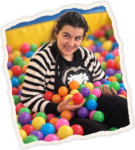 A young woman in a striped cardigan holding coloured balls in the ball pit