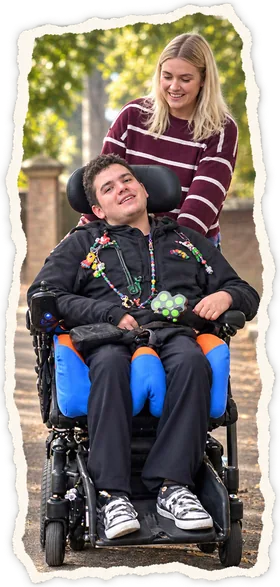 A member of staff walking a young man in his wheelchair outdoors