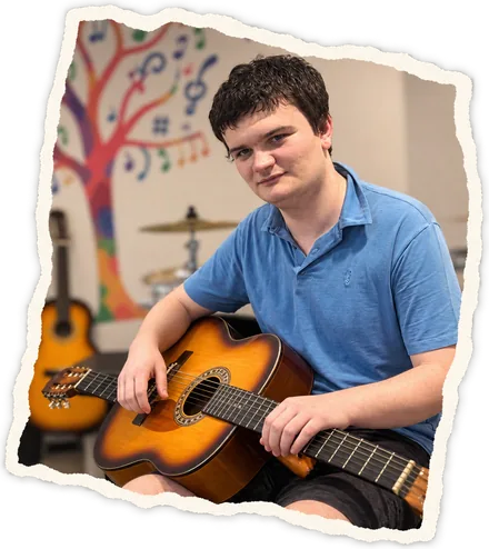 A young man in a blue polo shirt playing an acoustic guitar in the music room