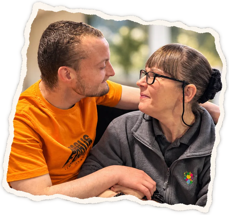 A man in an orange T-shirt and a member of staff smiling at each other, arm in arm