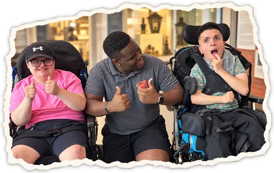Two people in wheelchairs and a member of staff giving a thumbs up together