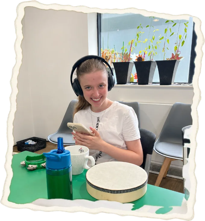 A young woman in headphones smiling at a table set with a drum and tambourine