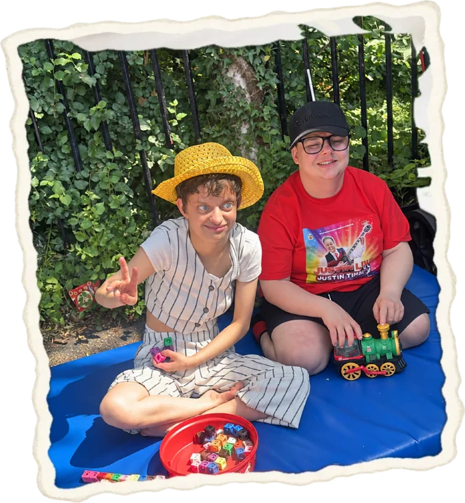 Two young people, one in a sun hat, playing with a toy train
