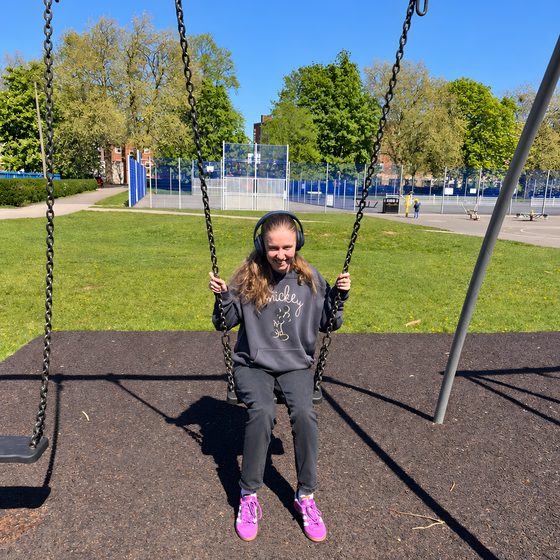 A member smiling on a swing in the park on a sunny day.