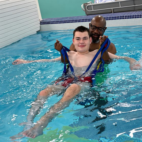 Two members supported by a staff member as they float and swim in the hydrotherapy pool.